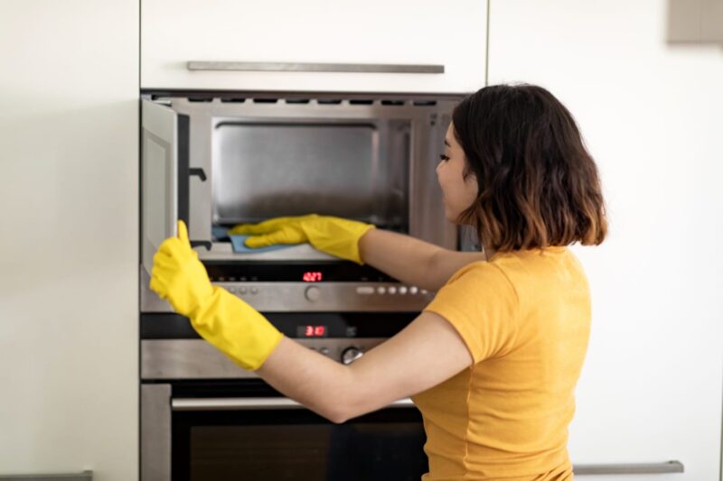 A maid is cleaning a microwave.
