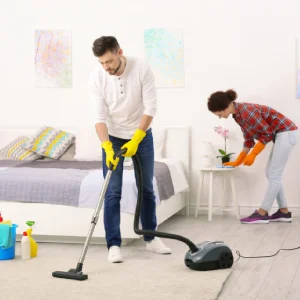 One maid is vacuuming, while the other is cleaning a bedside table.