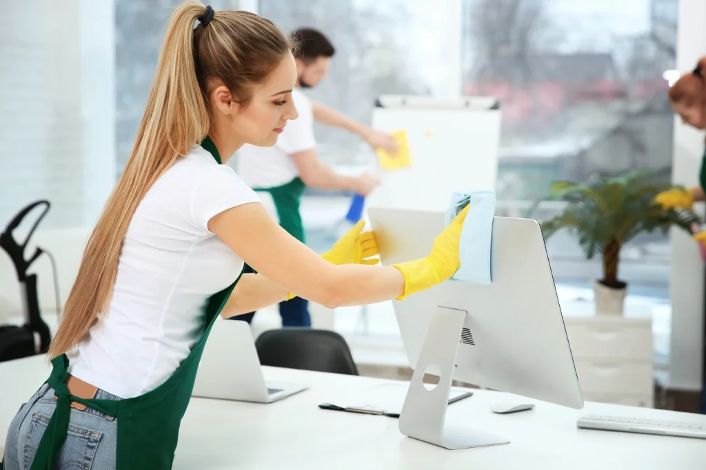 A maid is whiping the back of the computer.