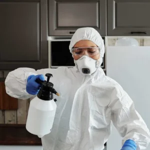 A maid dressed in protective gear is disinfecting the kitchen surface.